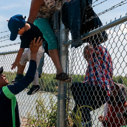 Migrants climb over a barbed wire fence after crossing the Rio Grande into US from Mexico, in Eagle Pass, Texas on August 25, 2023. (Photo by SUZANNE CORDEIRO / AFP) (Photo by SUZANNE CORDEIRO/AFP via Getty Images)